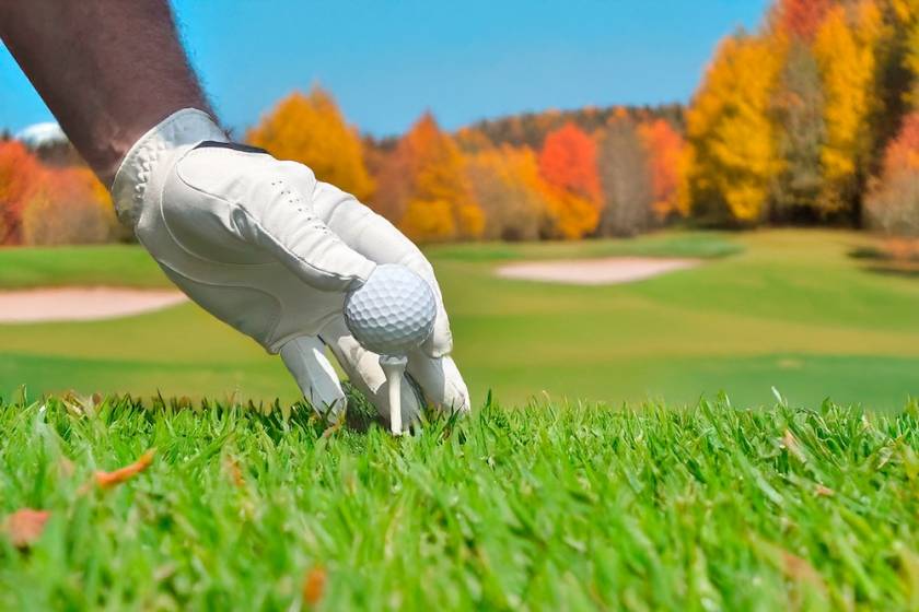 Golfer teeing up golf ball on hole of golf course in Autumn.