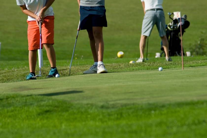 two young boys exercising on a green of golf course to pull the ball into hole,